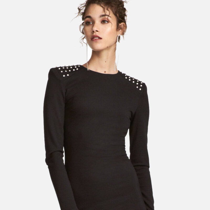Woman wearing a sleek black dress with studded shoulder details.