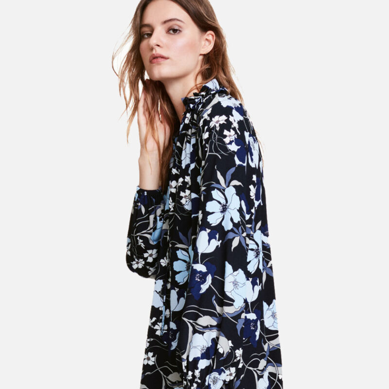 Woman wearing a black floral long-sleeve blouse posing sideways.