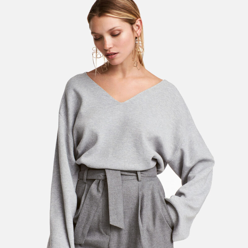 Woman wearing a light gray V-neck sweater and high-waisted gray pants.