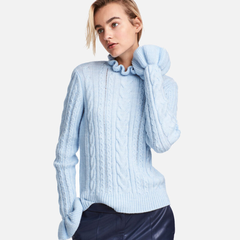 Woman wearing a light blue cable-knit sweater and dark pants.