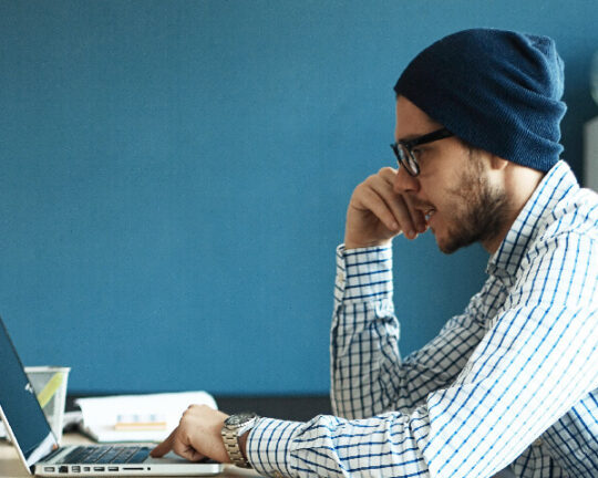 Man in beanie working on laptop.